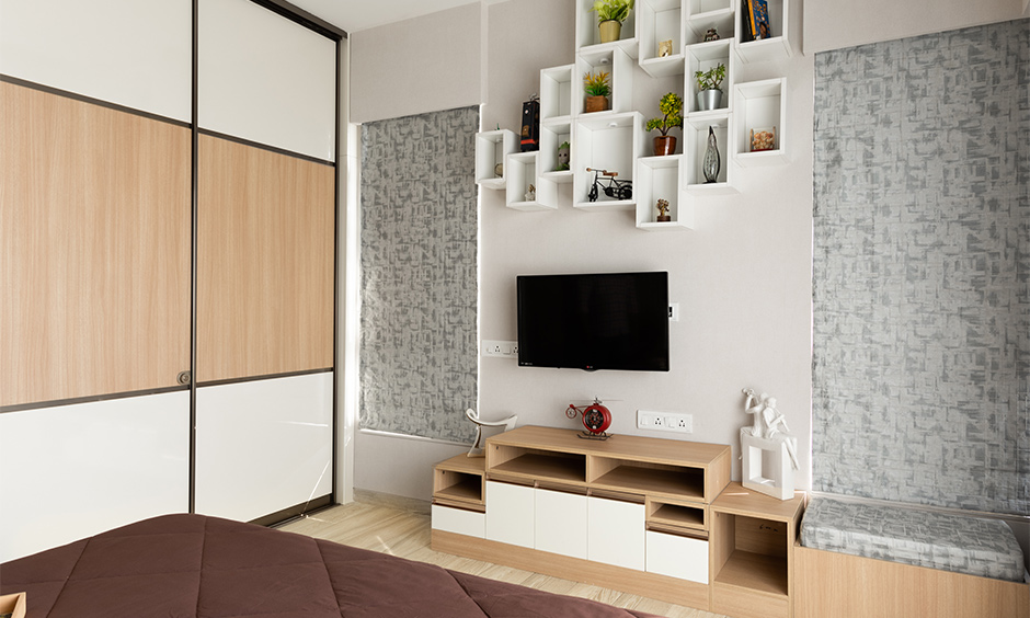 Bedroom with a unique wooden laminate TV unit with open shelves above designed by architects & interior designers in mumbai