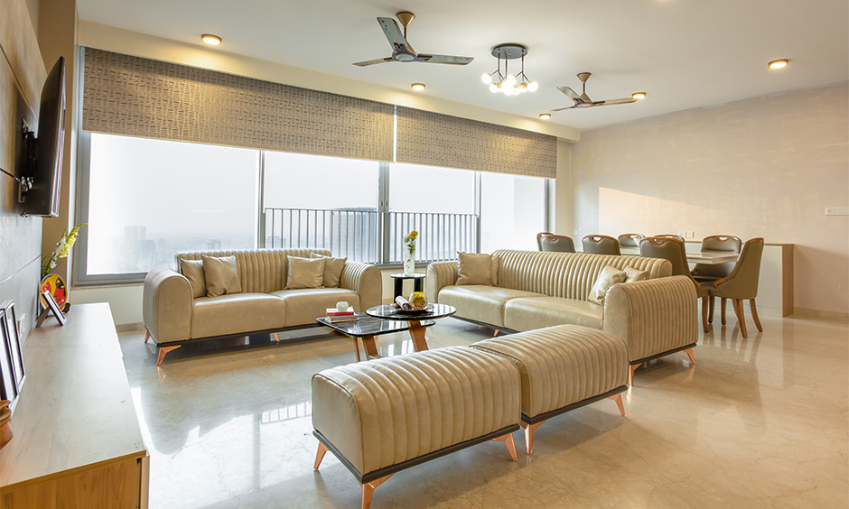 Best interior design in mumbai where living room is designed in with a neutral colour scheme, a leather sofa set and matching chairs for the dining table