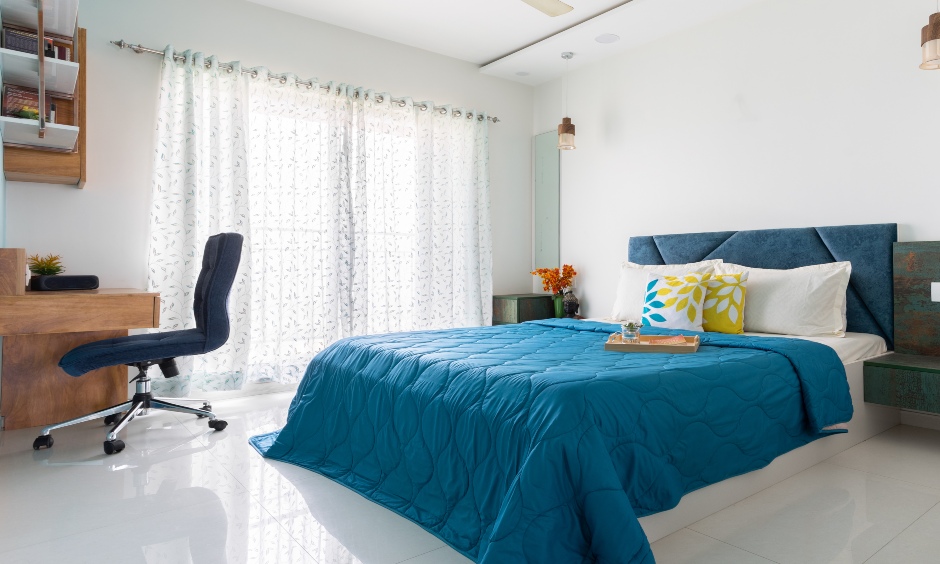 Master bedroom is designed in a white colour scheme, a king-size bed with teal cushioned headboard for home interiors mumbai