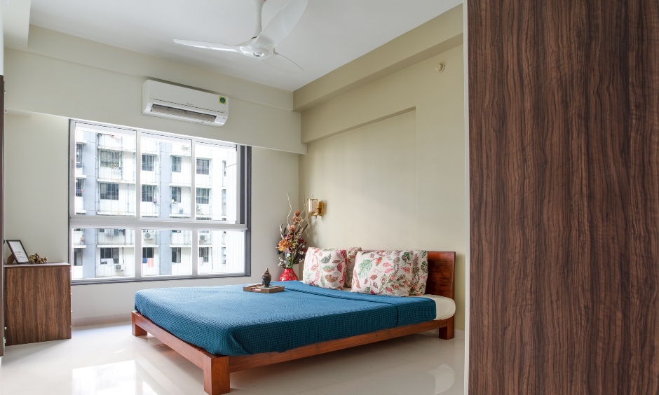 Master bedroom is decorated with a low lying wooden bed, a side table and high end interior designers in mumbai