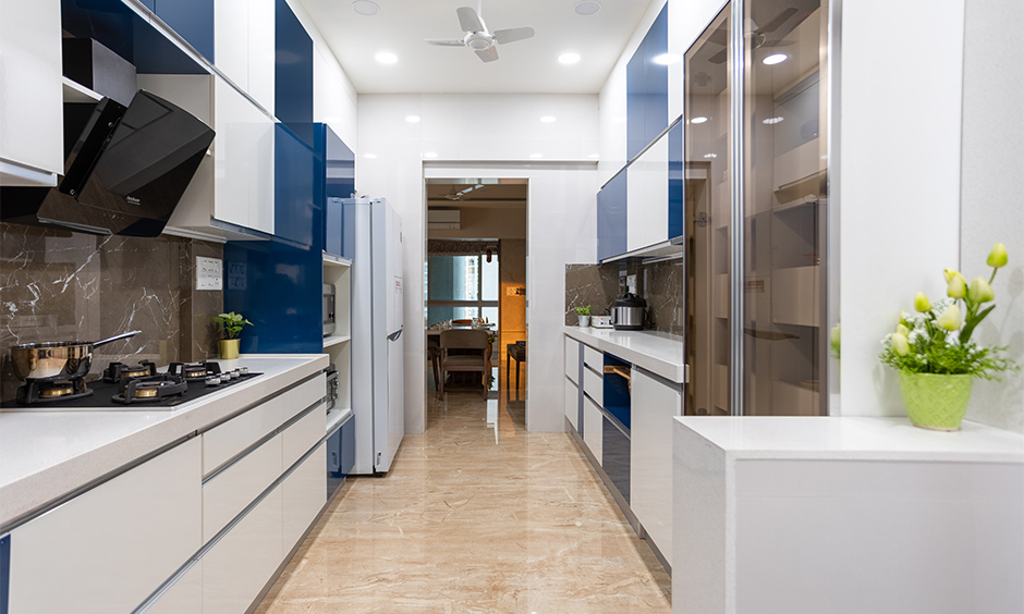 The parallel kitchen comes with glossy laminate cabinets, tall storage units designed by budget interior designers in mumbai
